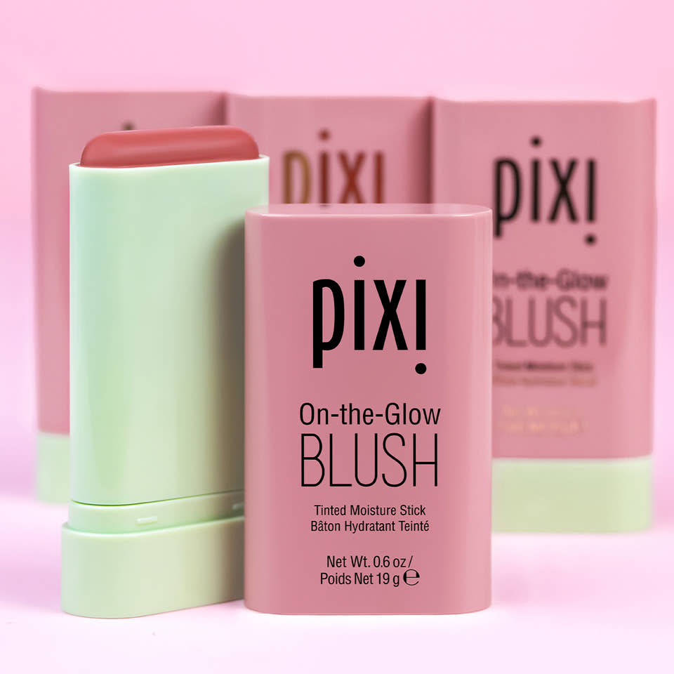 Pixi On-the-Glow Blush tinted moisturize shown with a pink product stick in front and two matching pink boxes behind it on a pink background. view 1
