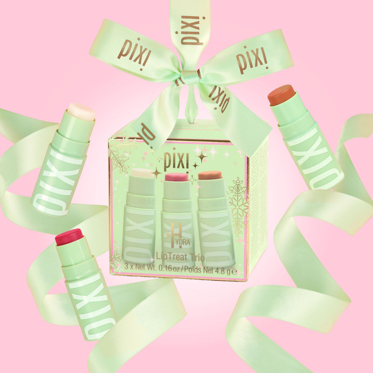 Pixi+Hydra LipTreat Trio gift set in a clear window box, wrapped in a mint green ribbon printed with the Pixi+ brand name, set against a solid pink background.