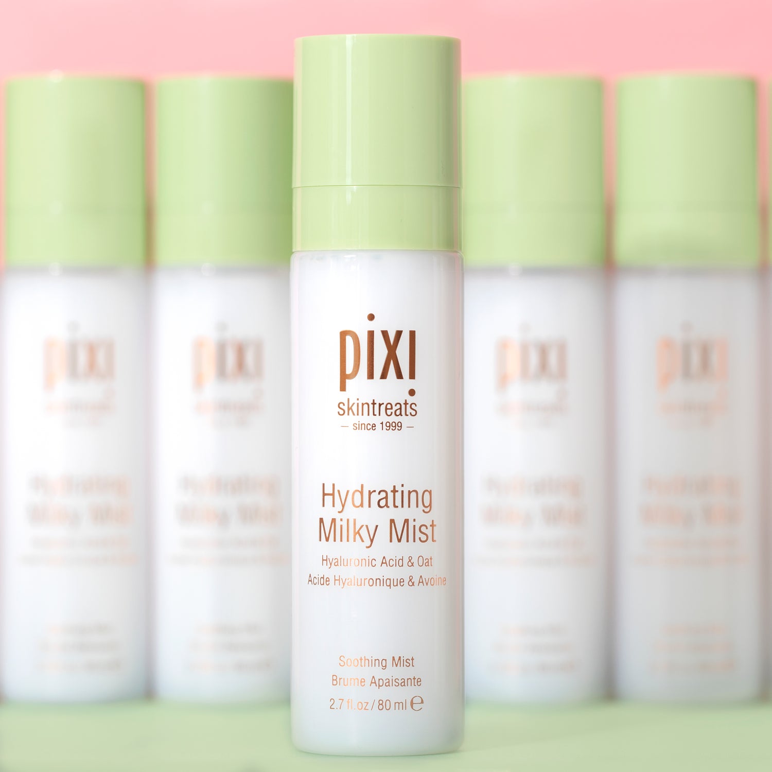 Row of Pixi skincare hydrating milky mist bottles on a pink background with shallow focus